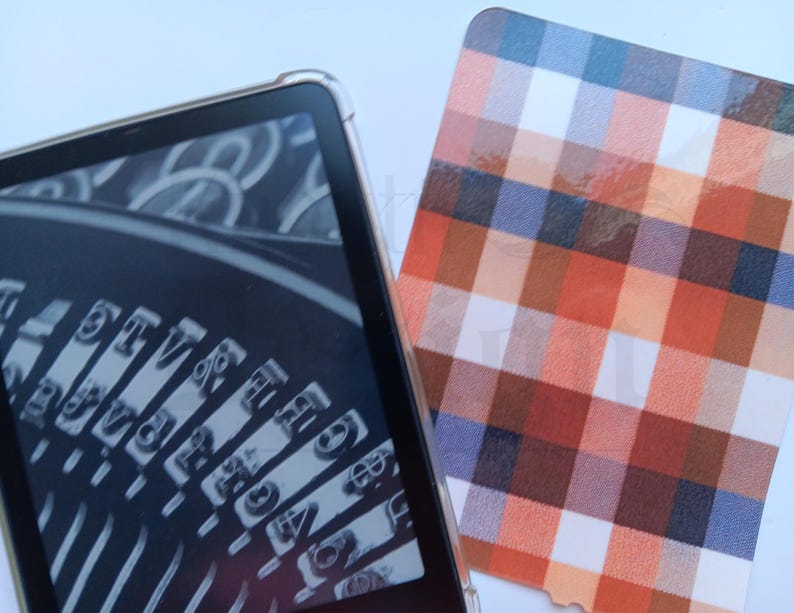 May include: A digital tablet in a clear case shows a monochrome image of typewriter keys. Next to it is a card with a plaid pattern in orange, red, blue, and white.