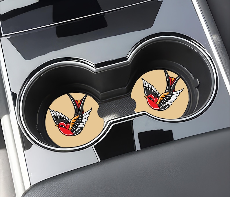 May include: Two beige car coasters with a vintage-style swallow tattoo design. The swallow is red, black, and yellow.