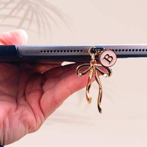 May include: A gold charm with a pink letter "B" and a gold bow hangs from a tablet.
