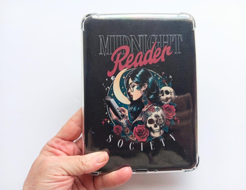 K&ouml;nnte beinhalten: Eine transparente Schutzh&uuml;lle mit einem schwarzen Grafikdesign. Das Design zeigt die Worte "MIDNIGHT Reader SOCIETY", eine lesende Frau, einen Mond, Rosen und Totenk&ouml;pfe. Die H&uuml;lle wird in einer Hand gehalten.