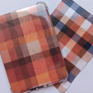 May include: A clear protective case and a matching card display a plaid pattern in shades of brown, orange, and white. The case is for a rectangular device, the card is a flat square.