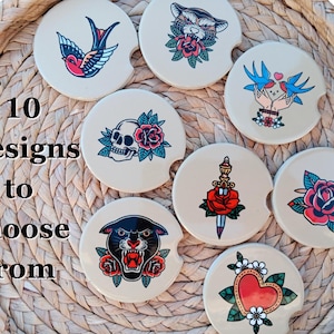 May include: Ten different designs of round drink coasters with various tattoo-inspired images. The coasters are beige with a white background and feature images of a skull, a panther, a rose, a dagger, a bird, a heart, and a cat. The text "10 Designs to choose from" is visible in the image.