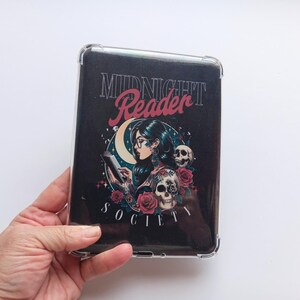 K&ouml;nnte beinhalten: Eine schwarze Tablet-H&uuml;lle mit einem Design, das eine lesende Frau, Totenk&ouml;pfe, Rosen und die Worte "Midnight Reader Society" zeigt. Die H&uuml;lle befindet sich in einer transparenten Schutzh&uuml;lle.
