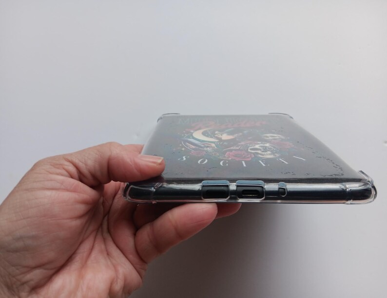 K&ouml;nnte beinhalten: Transparente Handyh&uuml;lle mit dunklem Hintergrund und floralem und Totenkopf-Design. Die H&uuml;lle hat einen Schutzsto&szlig;f&auml;nger und Aussparungen f&uuml;r die Anschl&uuml;sse und Tasten des Telefons. Der Text "SOCIETY" ist sichtbar.