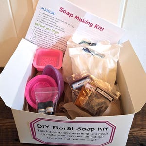 May include: A DIY Floral Soap Making Kit in a white box, containing instructions, pink silicone molds, essential oils, and natural ingredients. The kit includes lavender and jasmine soap making supplies. The box has a pink label with text.