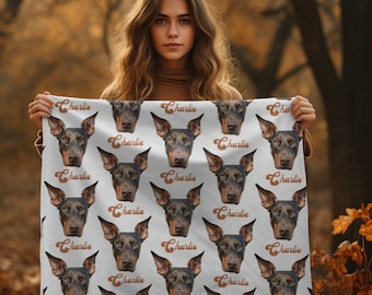 May include: A white fabric blanket with a repeating pattern of a brown and black dog's face. The dog's name, "Charlie", is written in a brown, retro font on the blanket.