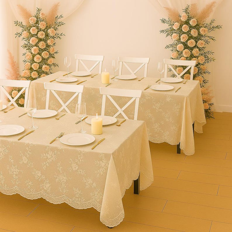 May include: A dining table setting with a cream-colored floral lace tablecloth, white plates, and gold-colored cutlery. White chairs are arranged around the table, with candles and wine glasses adding to the ambiance. Floral arrangements decorate the background.
