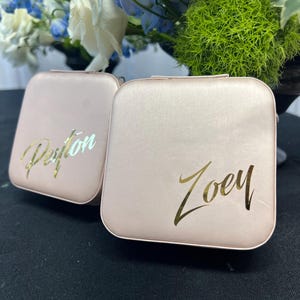 Pode incluir: Duas pequenas caixas quadradas cor-de-rosa com letras douradas. A caixa &agrave; esquerda diz "Peyton" e a caixa &agrave; direita diz "Zoey".