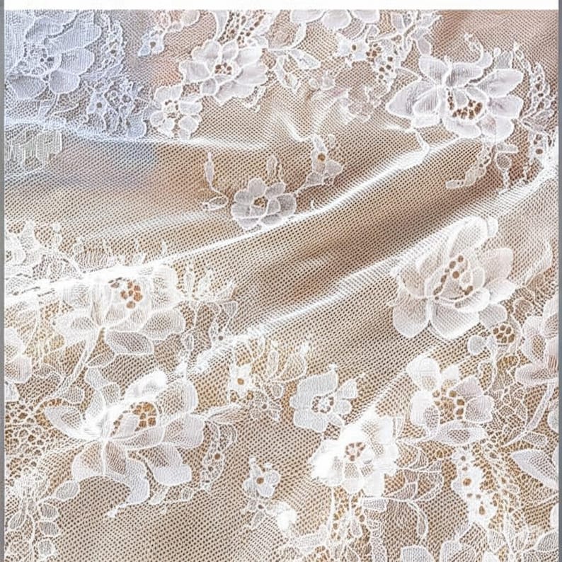 May include: Close-up of white floral lace fabric. The lace features a delicate pattern of flowers and leaves, with a fine net background. The fabric is slightly translucent, revealing a beige background.