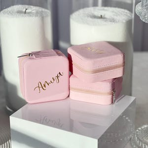 Pode incluir: Tr&ecirc;s caixas de joias de veludo rosa com letras douradas. As caixas est&atilde;o empilhadas uma em cima da outra. A caixa superior diz "Baby", a caixa do meio diz "Olivia" e a caixa inferior diz "Amruga".