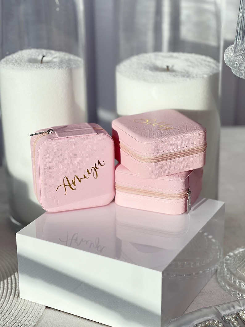 Pode incluir: Tr&ecirc;s caixas de joias de veludo rosa com letras douradas. As caixas est&atilde;o empilhadas uma em cima da outra. A caixa superior diz "Baby", a caixa do meio diz "Olivia" e a caixa inferior diz "Amruga".