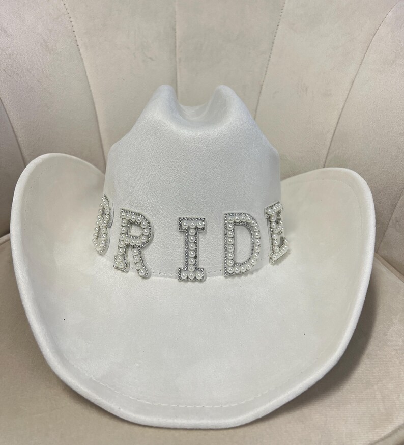 May include: White cowboy hat with the word "BRIDE" spelled out in pearl-embellished letters.