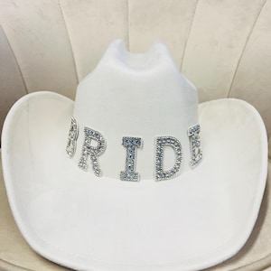 May include: White cowboy hat with the word "BRIDE" spelled out in rhinestones.