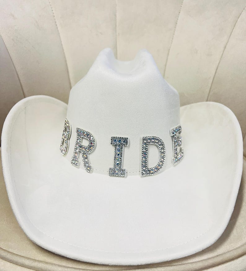 May include: White cowboy hat with the word "BRIDE" spelled out in rhinestones.