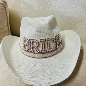 May include: White cowboy hat with a pink and white beaded "BRIDE" embellishment.