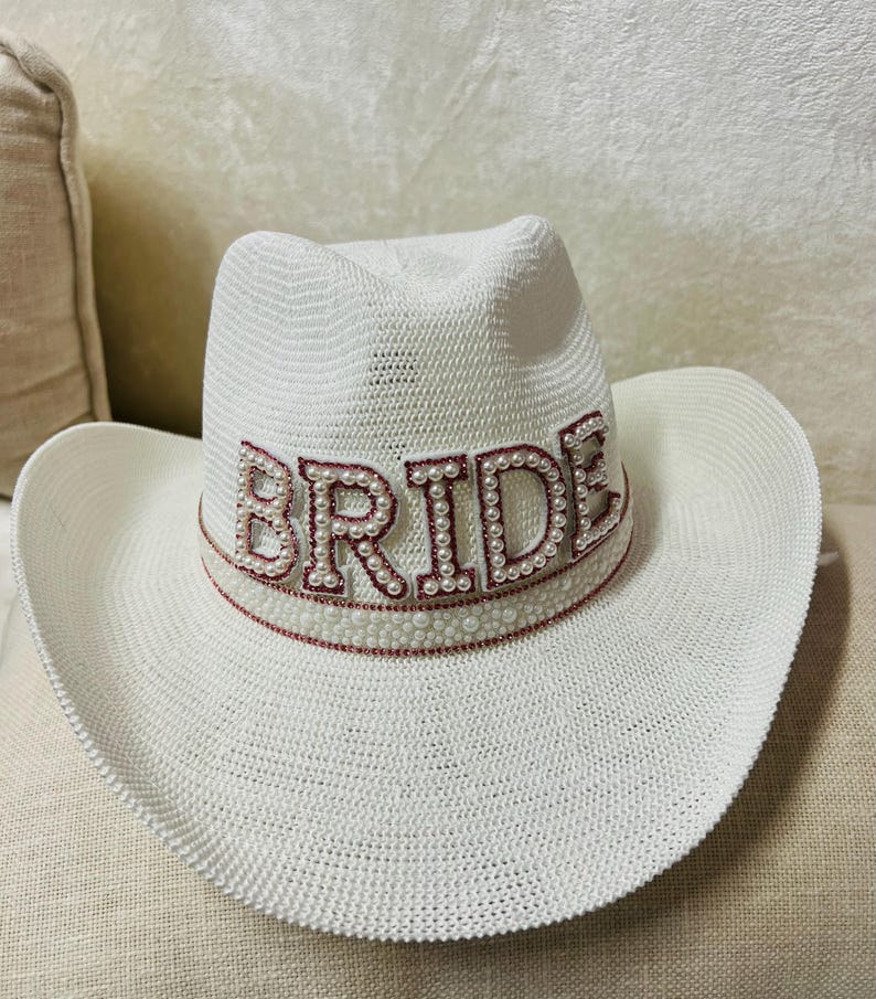 May include: White cowboy hat with a pink and white beaded "BRIDE" embellishment.
