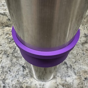 May include: A stainless steel tumbler with a purple silicone sleeve. The sleeve is positioned around the middle of the tumbler, providing a secure grip and a pop of color. The tumbler appears to be empty.