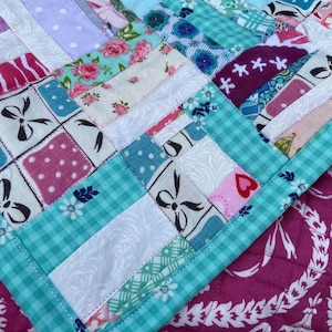 May include: A patchwork quilt with a variety of floral and geometric patterns in pink, blue, white, and green. The quilt is edged with a turquoise gingham fabric.
