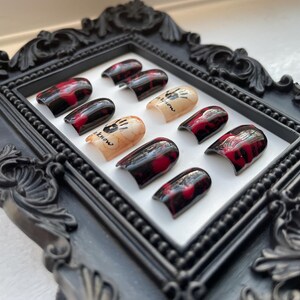 May include: A set of ten false nails with a black and red marbled design. The nails have a white handprint design with the text "It's show time" on them.