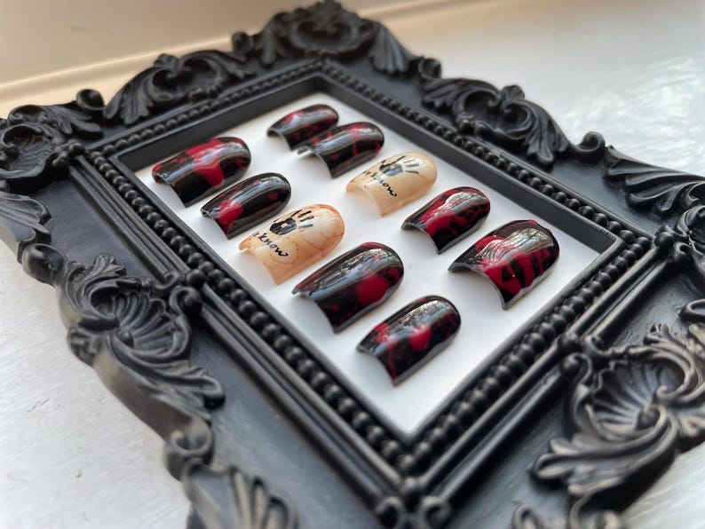 May include: A set of ten false nails with a black and red marbled design. The nails have a white handprint design with the text "It's show time" on them.