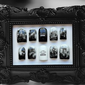 May include: A black and white display of press-on nails with a marble design. The nails have the words "HIDDEN" and "DETECTED" written on them.