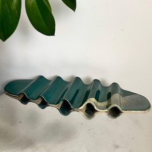 May include: A green ceramic soap dish with a wavy design. The dish has a white glaze on the bottom and is made of a textured material.