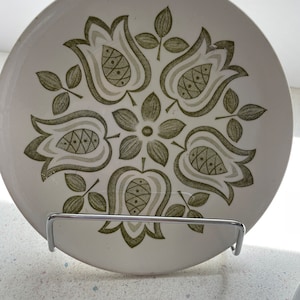 May include: A white ceramic plate with a green floral design. The design features stylized tulips and leaves.