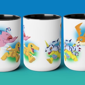 May include: A white ceramic mug with a black handle and interior rim, featuring a colorful graphic print of various Digimon characters including Biyomon, Agumon, Gabumon, and Patamon in action poses against a soft blue and green background.