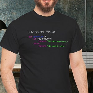 May include: A black t-shirt featuring a code snippet that reads "Introvert's Protocol" and includes the text "def greet_me():", "if you.see(me):", "return "Do not approach.", "else:", "return "No small talk."."