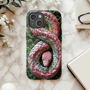 Pode incluir: Capa de smartphone com um design de cobra em mosaico. A cobra é retratada em tons de rosa, cinza e branco, enrolada sobre um fundo verde e cinza. A capa tem um acabamento brilhante e um recorte para a câmera.