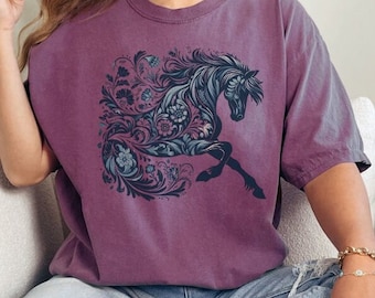 Op de afbeelding: Mauvekleurig T-shirt met een gedetailleerde illustratie van een paard. Het paard is versierd met bloemmotieven in blauw en teal. Het ontwerp is gecentreerd, waardoor een opvallende afbeelding ontstaat. Het T-shirt is een comfortabele, casual stijl.
