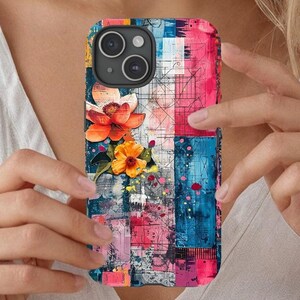 May include: A colorful phone case featuring a floral design with orange and yellow flowers. The case has a patchwork pattern with blue, pink, and white sections. The phone case is held by a person.