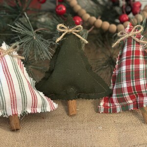 Pu&ograve; includere: Tre decorazioni natalizie a forma di albero in tessuto con bordi sfilacciati e tronchi fatti di bastoncini di cannella. Un albero presenta un motivo a righe bianche e rosse, uno &egrave; in feltro verde scuro e uno ha un design a quadri rossi, verdi e bianchi.
