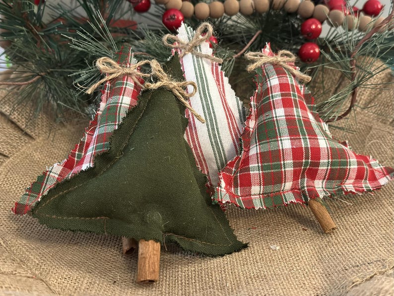Pu&ograve; includere: Tre decorazioni natalizie a forma di albero in tessuto con un mix di verde oliva tinta unita, motivi a quadri rossi e bianchi e righe. Ogni albero presenta bordi sfrangiati, un piccolo fiocco in spago di juta e un tronco in stecca di cannella.