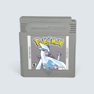Peut inclure: Une cartouche de jeu vidéo grise Nintendo Game Boy pour Pokémon Version Argent. L'étiquette présente le Pokémon Lugia, le logo Pokémon, un symbole de classification E, le texte DMG-APAE-USA et le texte This Side Out. Le haut est moulé.