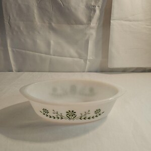 May include: White oval casserole dish with green floral and leaf design. The dish has two handles and is made of a thick, opaque material. The floral pattern is repeated around the rim of the dish.