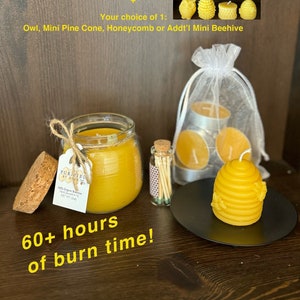 May include: A starter kit for making beeswax candles, featuring a 5 oz jar of honey-scented beeswax candle, a refillable matches bottle, six tealight candles, a heat-resistant candle plate, a mini beehive, and a choice of an owl, mini pine cone, honeycomb, or an additional mini beehive. The kit includes a label that reads "Purified By Bees" and "100% Organic Beeswax Hand Poured in the USA NET WT 5 oz". The text "60+ hours of burn time!" is also visible.