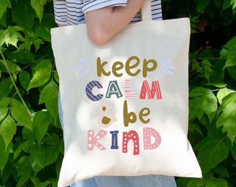 Könnte beinhalten: Eine weiße Canvas-Tragetasche mit dem Text "keep calm & be kind" in bunten, gemusterten Buchstaben. Die Buchstaben sind mit Herzen, Streifen und Punkten verziert.