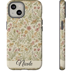 Puede incluir: Una funda floral para teléfono con una base de color crema y un estampado de flores y follaje rosas, amarillas y verdes. El nombre "Nicole" está impreso en cursiva en una banda de color crema en la parte inferior de la funda. La funda se muestra de frente y de lado.