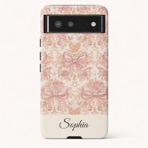 Puede incluir: Funda de teléfono con un estampado floral y de lazo en tonos rosa y crema. El diseño incluye motivos de lazo repetidos y elementos florales. El nombre "Sophia" está impreso en cursiva en la parte inferior.
