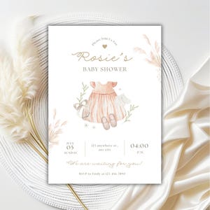May include: A baby shower invitation with a watercolor design. The invitation features the text "Rosie's BABY SHOWER" in elegant script, along with details for the event. The design includes a dress, shoes, and floral accents in soft peach and green hues.