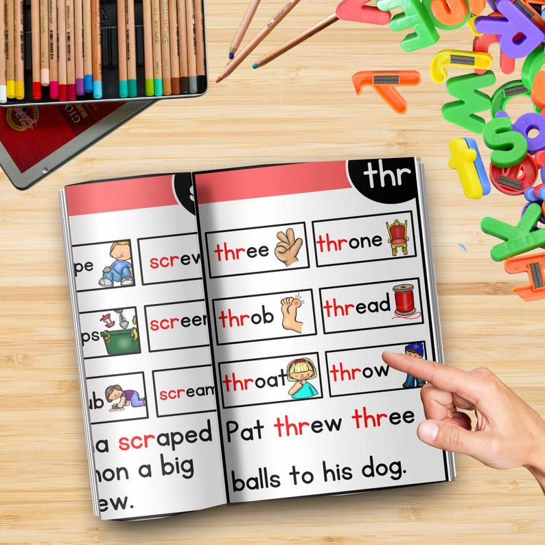 May include: An open book with colorful illustrations and text, including the word "thr" at the top. The pages display words like "three," "thread," and "throw," with corresponding images. Colored pencils and magnetic letters are scattered around.