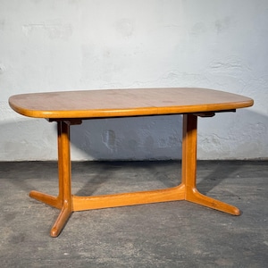 May include: A rectangular wooden dining table with rounded corners and a smooth, light brown grain finish. The table features a central support structure with two vertical legs connected by a horizontal base bar that extends into four feet.
