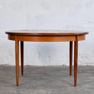 Peut inclure: Table ronde en bois de style moderne du milieu du siècle, avec quatre pieds effilés. Le plateau est de couleur brun clair, et les pieds et la ceinture sont d'une nuance de brun plus foncée. La table mesure environ 76 cm de diamètre.