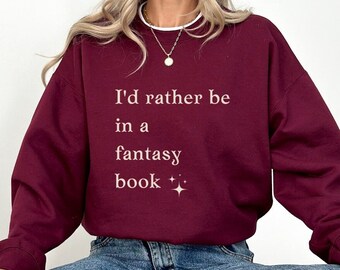 May include: A maroon sweatshirt with the text "I'd rather be in a fantasy book" printed on the front. The text is in a white font with a small sparkle design.