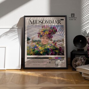May include: A framed movie poster for the film "Midsommar" featuring a woman wearing a flower crown and a floral dress. The poster is black framed and has a white background with the movie title in black text. The poster also includes the movie's rating, runtime, and release date.