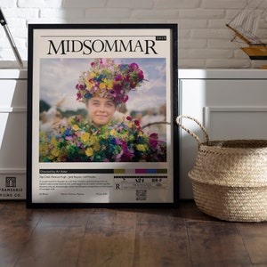 May include: A movie poster for the film "Midsommar" (2019) featuring a young woman wearing a flower crown and a floral dress. The poster is framed in black and has a white background with the film title and director's name printed in black.