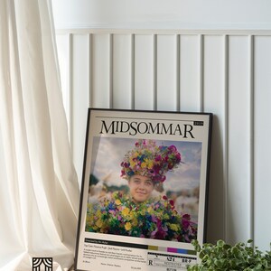 May include: A movie poster for the film "Midsommar" featuring a woman wearing a flower crown and a floral dress. The poster is framed in black and has a white background. The text on the poster reads "Midsommar" and "2019".