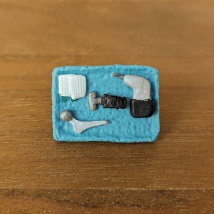 May include: A blue square tile with a white, black, and silver design. The design includes a drill, a wrench, a bolt, and a piece of paper.