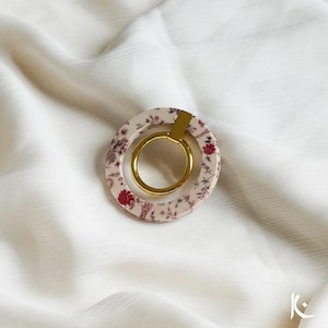 Op de afbeelding: Een ronde oorbel met een bloemenpatroon en een gouden ring in het midden. De oorbel is gemaakt van hars en heeft een delicaat bloemenpatroon in roze en rode tinten.